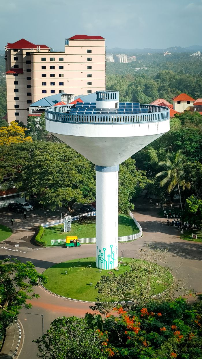 Aerial view of a modern water tower with solar panels surrounded by lush greenery and buildings.